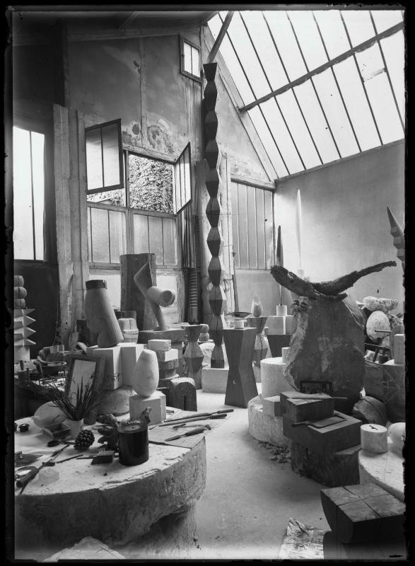 Constantin Brancusi, Vue d'ensemble de l'atelier. On aperçoit les œuvres Le Baiser (1923-1925), La Colonne sans fin I (v. 1925), Colonne du Baiser (1916-1917), L'Oiseau dans l'espace, bronze poli (1924), L'Oiseau dans l'espace, marbre blanc (1925), Le Crocodile, Socles, vers 1926 © Succession Brancusi - All rights reserved (Adagp) Centre Pompidou, Mnam-Cci/Dist. Rmn-Gp