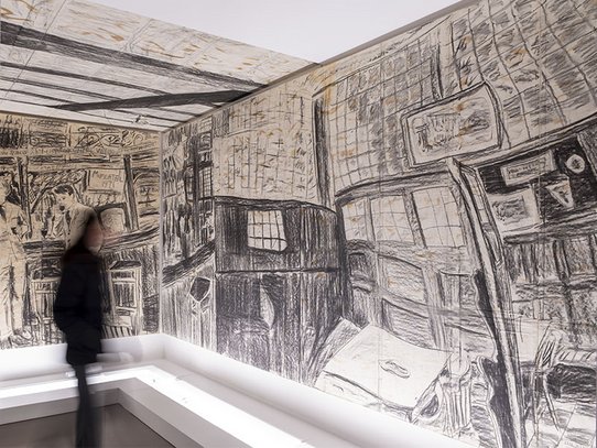 In a room entirely covered with charcoal drawings, a visitor explores “The Bar n°1,” a monumental work by Gilbert & George. The walls and ceiling form an immersive black-and-white mural depicting a detailed, expressive London bar interior. The ambiance merges the familiarity of a social setting with the surreal distortion of memory. The scale and warped perspective fully absorb the viewer into a life-sized graphic world.