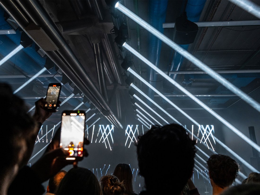 Sous une structure industrielle brute, la foule vit l’intensité sonore et visuelle du concert de Justice. Des lignes de lumière blanche, signature du duo, tranchent l’espace avec une précision millimétrée. Les téléphones s’élèvent pour immortaliser l’instant. L’ambiance est électrique, presque liturgique, typique des lives immersifs de Justice, entre énergie brute et esthétique futuriste
