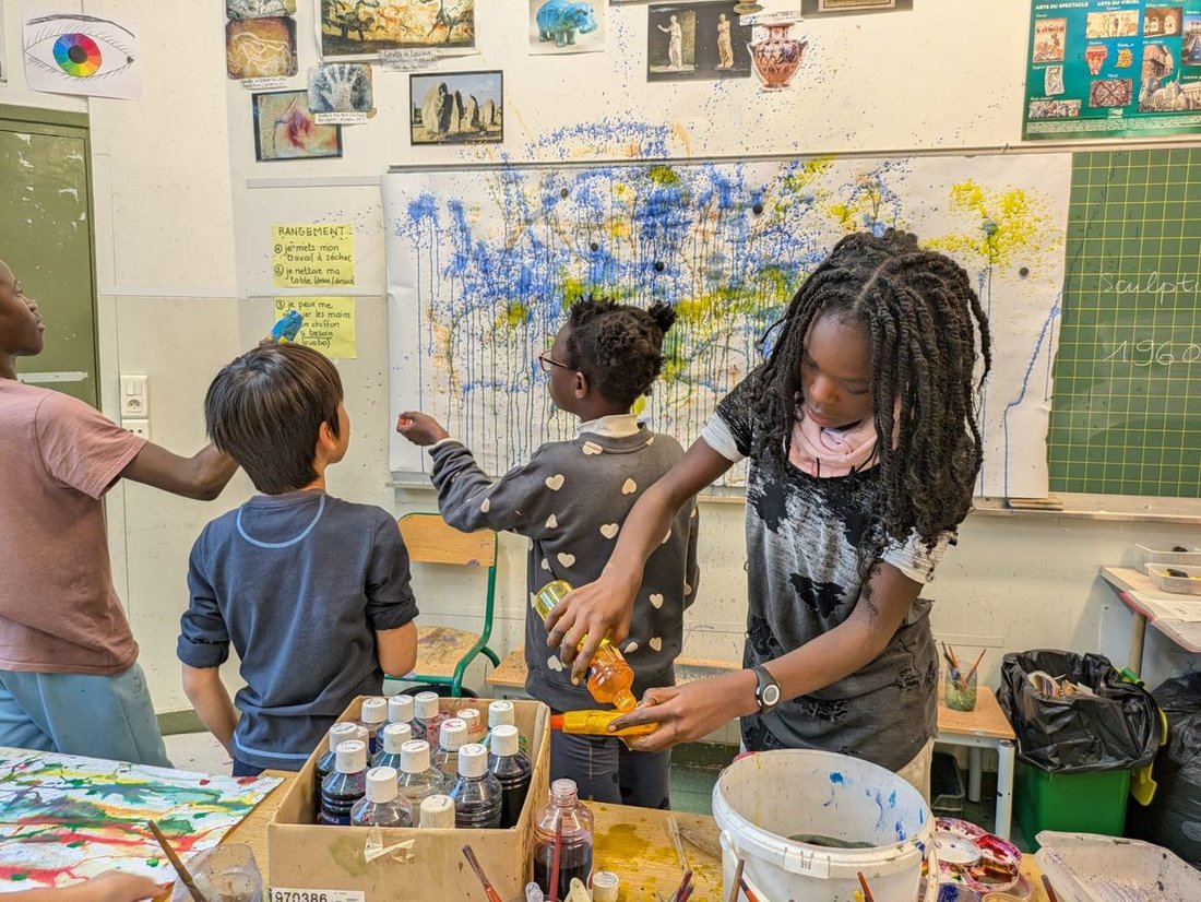 Atelier de pratique artistique à l'école : groupe d'enfants en train de peindre un tableau abstrait à coups de jets de peinture