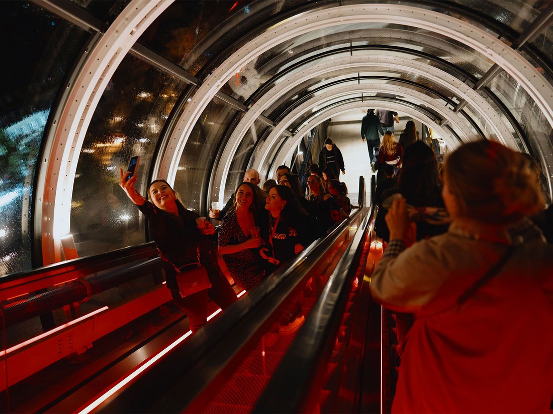 Dans la célèbre chenille du Centre Pompidou, baignée d’une lumière rouge vive, les visiteurs se pressent et immortalisent l’instant. Des rires résonnent, des selfies s’échangent, créant une ambiance joyeuse et collective typique de la soirée "Because Beaubourg". À travers les vitres courbes, les lumières nocturnes de Paris scintillent, ajoutant une touche magique à ce moment suspendu entre architecture emblématique et fête culturelle.