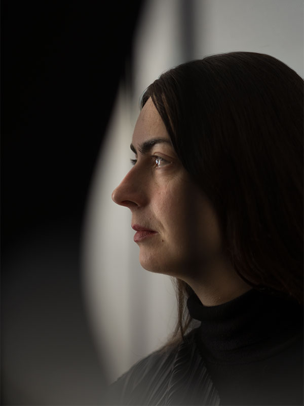 Ce portrait photographique de Jeanne Vicérial, réalisé par Pierre Malherbet, capture l’artiste dans une posture calme et contemplative. Photographiée de profil, elle se détache sur un fond sobre où alternent ombre profonde et lumière diffuse. La douceur de l’éclairage souligne les traits de son visage, son regard concentré et la texture sombre de ses vêtements plissés. Le cadrage épuré crée une atmosphère silencieuse et introspective, laissant toute la place à l’expression et à la présence de l’artiste. Les contrastes délicats entre obscurité et lumière donnent à l’image une dimension presque cinématographique. Ce portrait évoque à la fois la sensibilité créative, la réflexion intérieure et l’élégance contemporaine associées à l’univers textile et sculptural de Jeanne Vicérial.